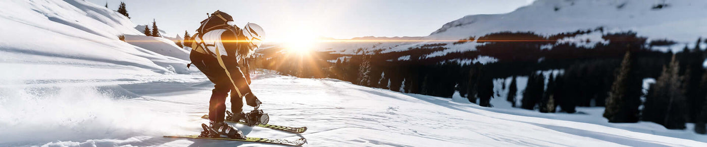 Skier gliding down snowy slope at sunset, surrounded by winter landscape and trees.