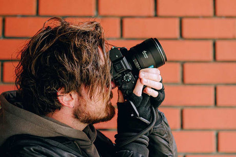 Photographer using a camera with an 85mm lens against a brick wall, focused on capturing portraits.