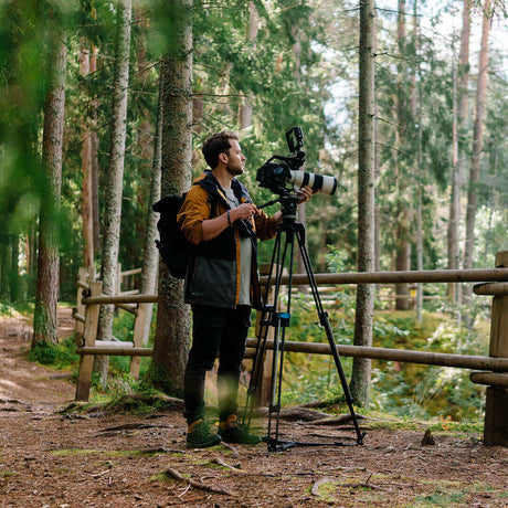 Photographer setting up a camera on a tripod in a lush forest for jungle photography.
