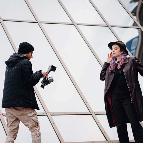 Photographer capturing a model in fashionable attire against a modern glass architectural backdrop.