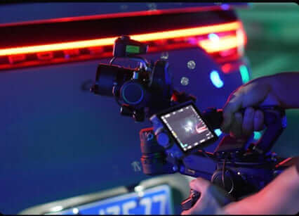 Close-up of a hand holding a camera gimbal while filming a car with neon lights.
