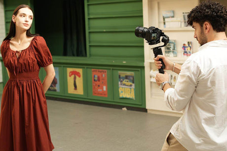 Photographer using a gimbal stabilizer to capture sharp images of a model in a stylish dress in a studio setting.