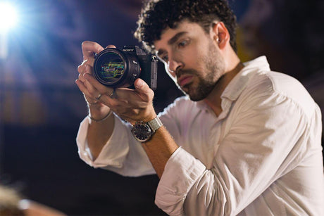 Person holding a camera with a focused expression, capturing still life photography in a creative environment.