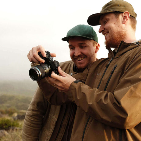 Two photographers reviewing images on a camera in a foggy outdoor setting, smiling and enjoying their time.