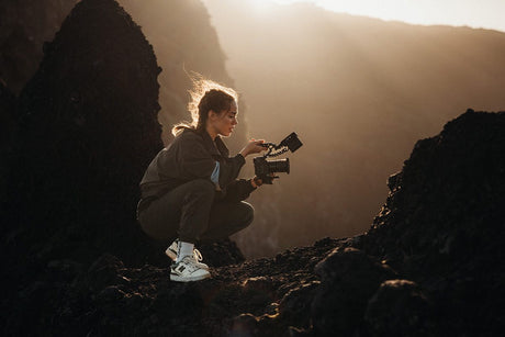Photographer crouches on rocky terrain capturing images during golden hour in a stunning landscape.