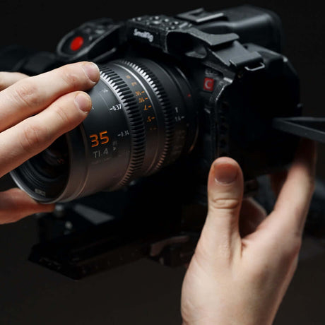 Close-up of a photographer's hands adjusting a camera lens with a 35mm focal length.