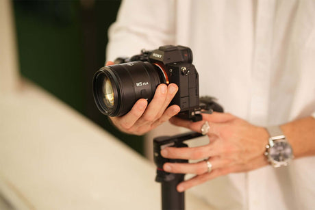 Photographer holding a Sony camera with an 85mm lens on a stabilizer for video shooting.