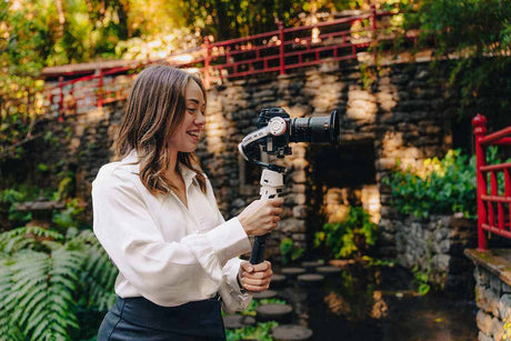Woman using a camera stabilizer in a lush outdoor setting, showcasing videography skills.