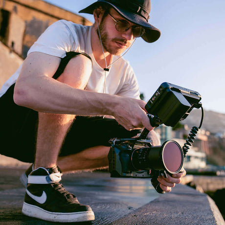Photographer adjusting camera settings while crouched outdoors in a sunny setting.