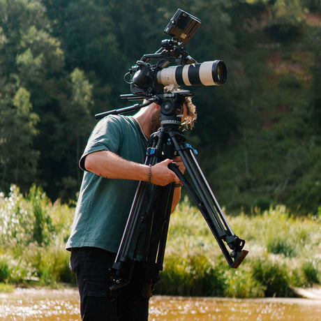 Photographer using a tripod with a large camera lens near a serene outdoor setting.