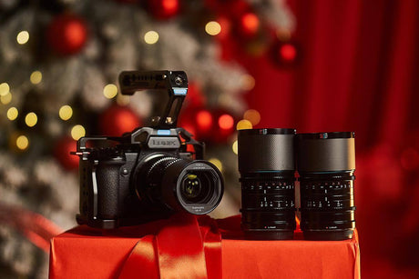 Camera and lenses on a red gift box with holiday decorations in the background, perfect for content creators.