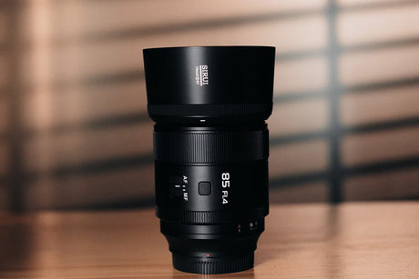 Close-up of an 85mm f/1.4 camera lens with a lens hood, placed on a wooden surface with soft lighting.