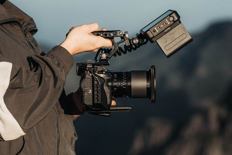 Close-up of a photographer holding a camera with a monitor and lens, showcasing equipment for low angle shots.