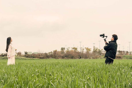 Photographer using a camera gimbal to capture a model in a green field on an overcast day.