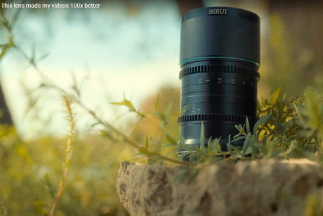 A close-up of a Sirui camera lens resting on a rock surrounded by greenery, highlighting its quality for video enhancement.