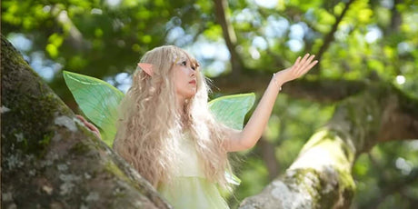 Fairy character with long hair and green wings perched on a tree branch in a lush forest.