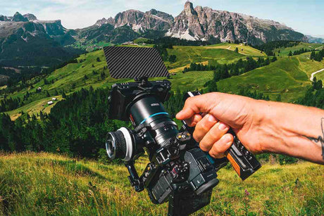 Close-up of a hand holding a professional camera on a mountain landscape background.