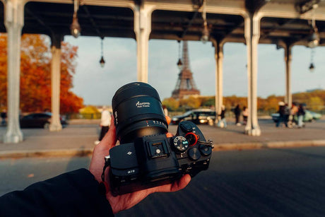 Hand holding a camera with a lens in front of the Eiffel Tower during autumn, perfect for capturing sports activities.