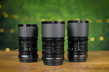 Three camera lenses on a wooden table, set against a softly blurred green background with decorative lights.