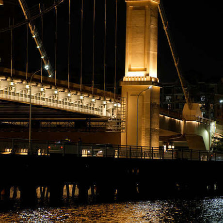 Beautifully illuminated bridge at night, showcasing its architectural details and reflections in the water.