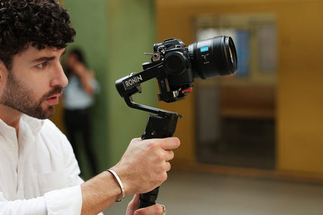 Man using a gimbal stabilizer to capture video with a DSLR camera in an indoor setting.