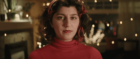 Close-up of a woman in a red turtleneck with festive lights blurred in the background, exuding a warm, inviting atmosphere.