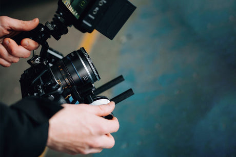 Close-up of a photographer's hands adjusting a camera lens with stabilizer equipment.