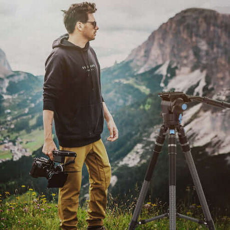 Photographer outdoors with a camera and tripod, showcasing ideal gear for capturing landscapes.