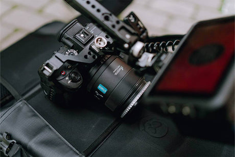 Close-up of a small camera with a zoom lens placed on a black bag, showcasing its compact design and features.